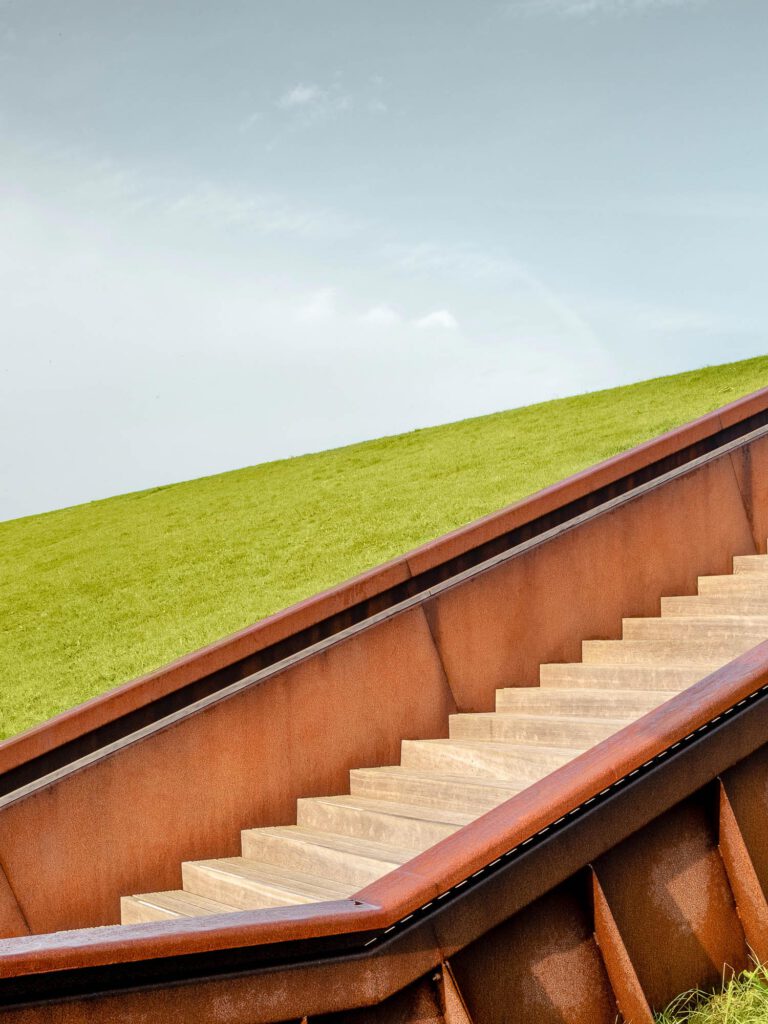 Fotografie van landschapsarchitectuur in Noord-Holland, die een trap van cortenstaal en hout op een dijk laat zien.